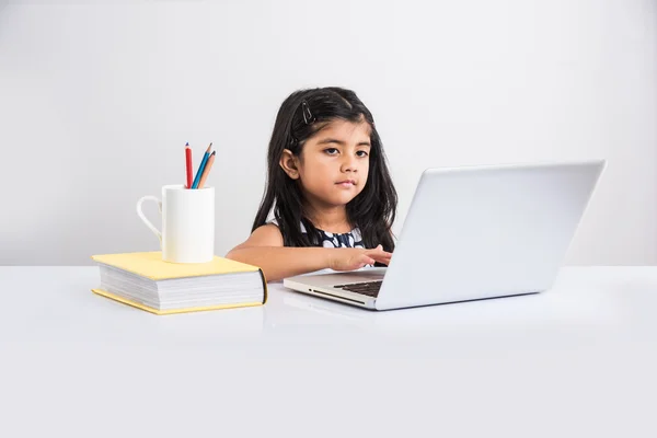 cheerful indian little girl using laptop, asian small girl playing on laptop, isolated over white background, cute indian baby girl playing on laptop over study table