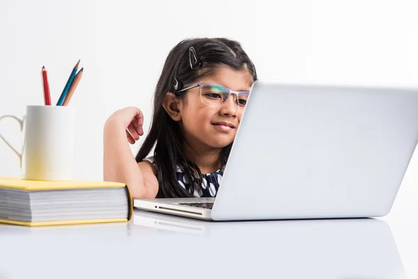 cheerful indian little girl using laptop, asian small girl playing on laptop, isolated over white background, cute indian baby girl playing on laptop over study table