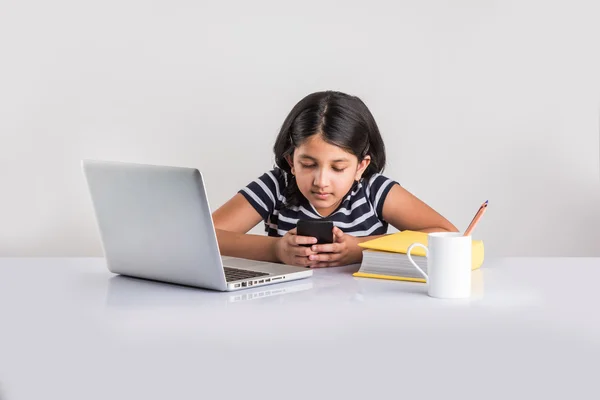노트북에서 공부하는 동안 스마트 폰을 사용하여 귀여운 작은 인도 소녀 — 스톡 사진