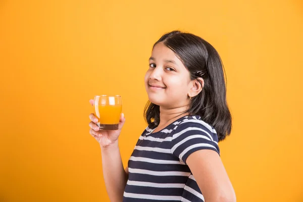 Portret van Indiase klein meisje het drinken van mango sap of vruchtensap in een glas, Aziatisch meisje en een glas sap, Indiase kleine meisje houden een glas mango sap of sinaasappelsap op gele achtergrond — Stockfoto