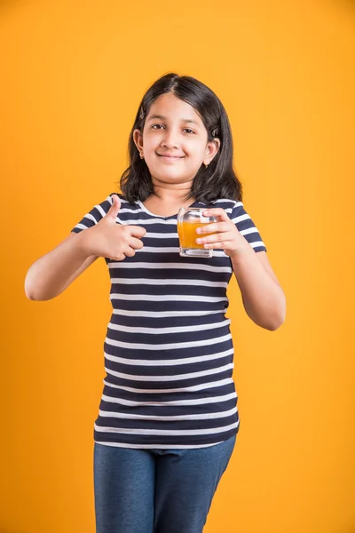 Portret van Indiase klein meisje het drinken van mango sap of vruchtensap in een glas, Aziatisch meisje en een glas sap, Indiase kleine meisje houden een glas mango sap of sinaasappelsap op gele achtergrond — Stockfoto