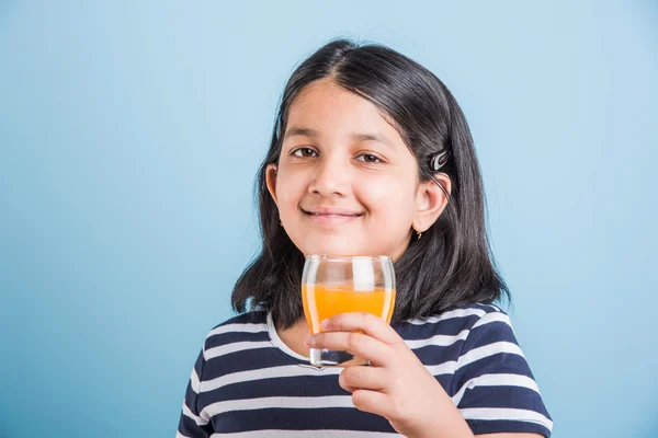 Portret van Indiase klein meisje het drinken van mango sap of vruchtensap in een glas, Aziatisch meisje en een glas sap, Indiase kleine meisje houden een glas mango sap of sinaasappelsap op blauwe achtergrond — Stockfoto