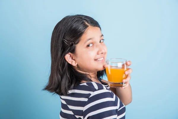 Portret van Indiase klein meisje het drinken van mango sap of vruchtensap in een glas, Aziatisch meisje en een glas sap, Indiase kleine meisje houden een glas mango sap of sinaasappelsap op blauwe achtergrond — Stockfoto