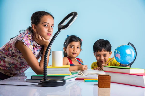 three cute indian kids studying, smart asian girls and boy doing home work, indian siblings studying, indian small girl helping her brother and sister in doing homework