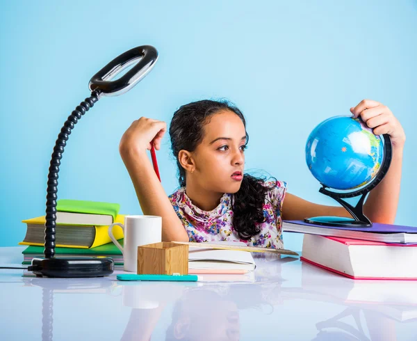 Estudiante de chica india mirando globo educativo y sentado en la mesa con libros, lámpara de mesa y taza de leche, niña asiática estudiando geografía, chica asiática curiosa estudiando geografía con globo — Foto de Stock