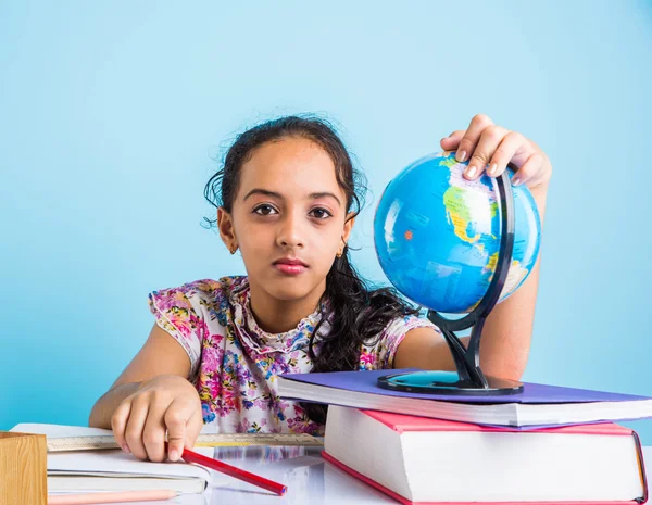 Estudiante de chica india mirando globo educativo y sentado en la mesa con libros, lámpara de mesa y taza de leche, niña asiática estudiando geografía, chica asiática curiosa estudiando geografía con globo — Foto de Stock