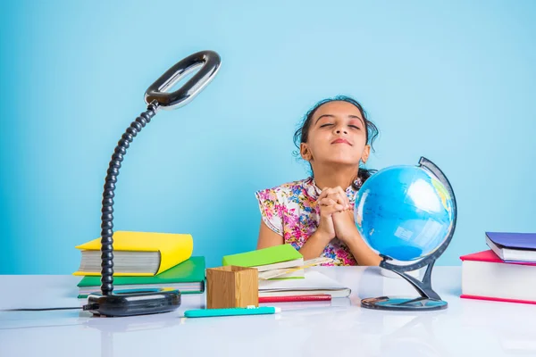 education and home concept - stressed student girl with books, indian girl child tired of studying or doing homework, asian girl studying and stressed, with globe toy and coffee mug