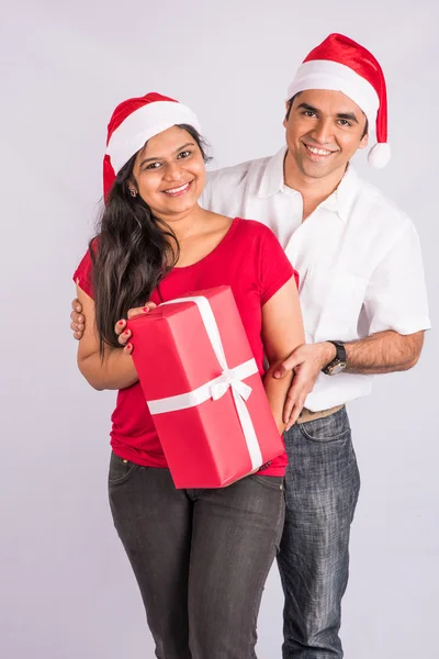 young indian couple smiling with with christmas gift, asian couple and christmas gift, with santa hat, white background, india and christmas celebration, christmas gift and indian couple, isolated