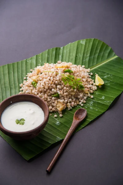 Sabudana Khichadi - An authentic dish from Maharashtra made with sago seeds served over coconut leaf with curd in a wooden bowl