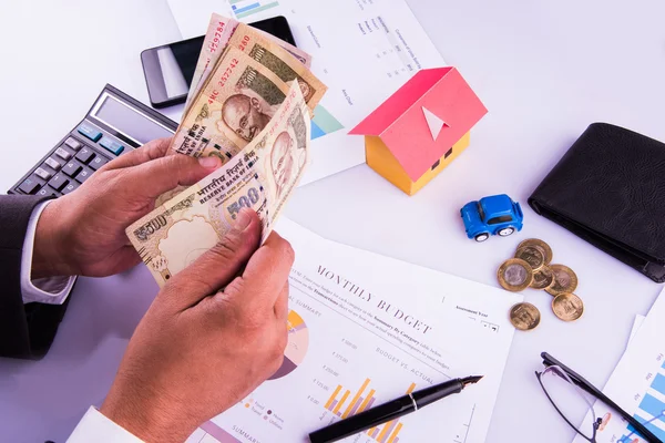 Hombre indio o contable persona que presenta formulario de declaración de impuestos indio o documento ITR que muestra moneda india, modelo de casa, coche de juguete y calculadora sobre mesa blanca, enfoque selectivo —  Fotos de Stock