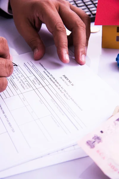 Hombre indio o contable persona que presenta formulario de declaración de impuestos indio o documento ITR que muestra moneda india, modelo de casa, coche de juguete y calculadora sobre mesa blanca, enfoque selectivo — Foto de Stock