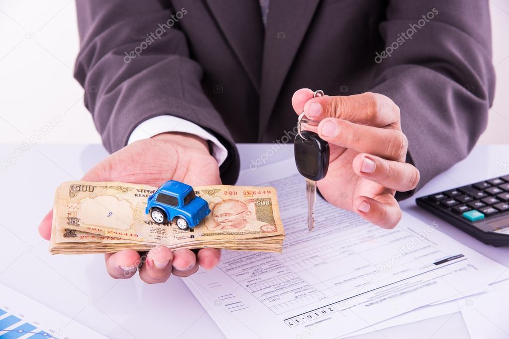 indian businessman holding currency notes and toy car with key, buying car concept