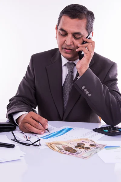 Indian man or accountant person filing Indian income tax returns form or ITR document showing indian currency, house model, toy car and calculator over white table top, selective focus