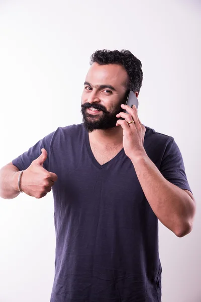 Hipster indyjski młody człowiek z brodą i wąsy zajęty za pomocą smartfona, izolowane na białym tle — Zdjęcie stockowe