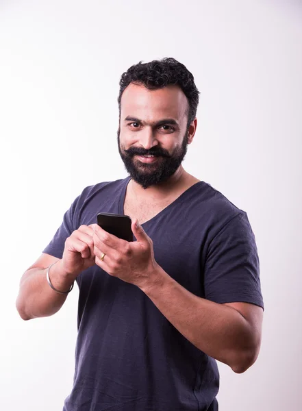 Hipster indiana jovem com barba e bigode ocupado usando smartphone, isolado sobre fundo branco — Fotografia de Stock