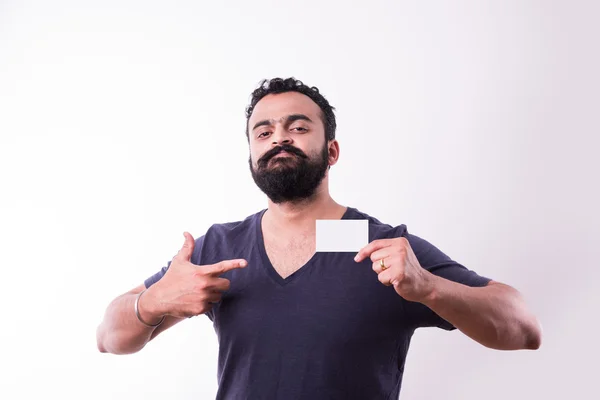 Jovem indiano hipster com barba e bigode exibindo cartão de visita vazio. feliz sorriso jovem bonito asiático cara desgaste camisa isolado branco fundo — Fotografia de Stock