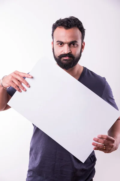 Retrato de homem indiano bonito com barba segurando placa branca em branco. homem indiano segurando cartaz em branco . — Fotografia de Stock