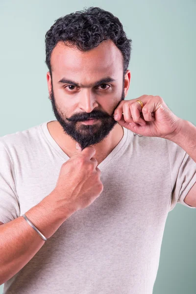 Indiase jonge man aanraken baard-groene achtergrond — Stockfoto