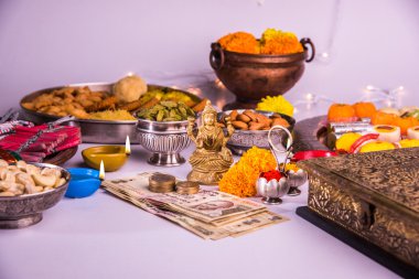 oil lamp or diya with crackers, sweet or mithai, dry fruits, indian currency notes, marigold flower and statue of Goddess Laxmi or lakshmi on diwali night clipart