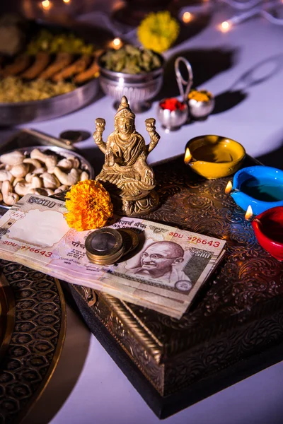 石油ランプやクラッカーと甘いかは mithai、ドライ フルーツ、インドの通貨のノート、マリーゴールドの花と女神ラクシュミのディワリの夜にラクシュミ像 diya — ストック写真