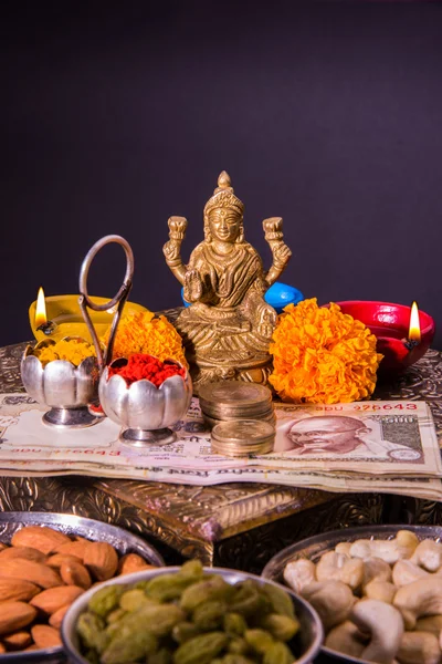 Lámpara de aceite o diya con galletas, dulces o mithai, frutas secas, billetes de moneda india, flor de caléndula y estatua de la Diosa Laxmi o lakshmi en la noche diwali — Foto de Stock