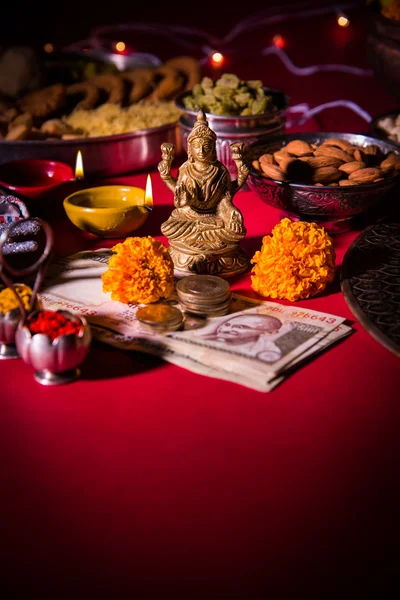 Oil lamp or diya with crackers, sweet or mithai, dry fruits, indian currency notes, marigold flower and statue of Goddess Laxmi or lakshmi on diwali night — Stock Photo, Image