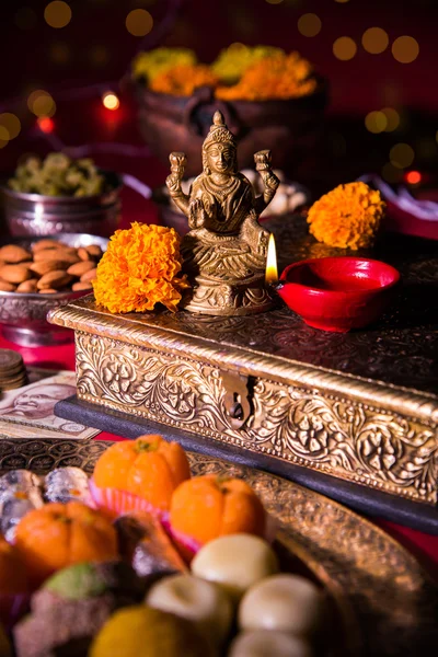 Lámpara de aceite o diya con galletas, dulces o mithai, frutas secas, billetes de moneda india, flor de caléndula y estatua de la Diosa Laxmi o lakshmi en la noche diwali — Foto de Stock