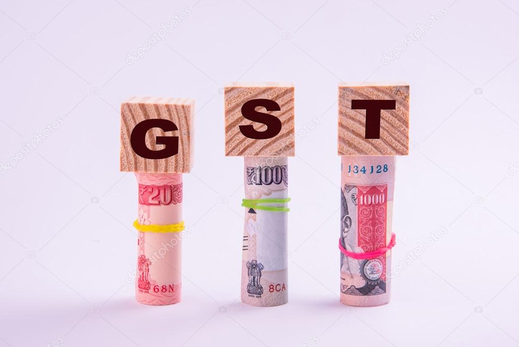 wooden cubes with GST text written over it placed over 3 rolls of indian currency notes, isolated over white background