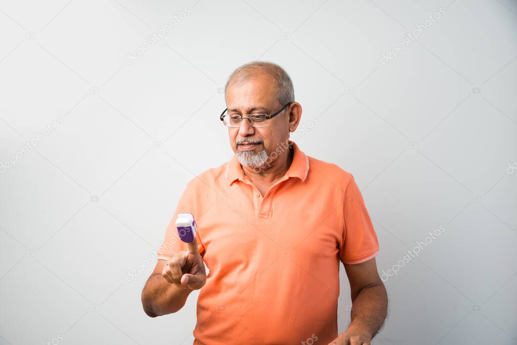Indian asian senior or old man checking temperature using thermometer and oxygen saturation using oximeter