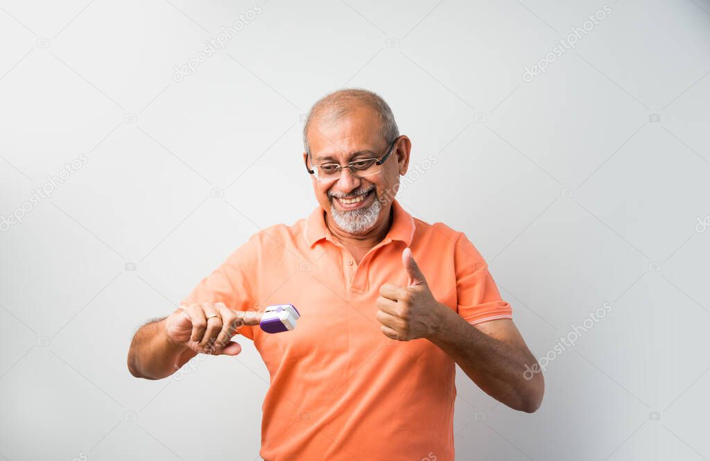 Indian asian senior or old man checking temperature using thermometer and oxygen saturation using oximeter