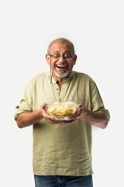 stock image Indian asian old or retired senior man eating potato chips on white background