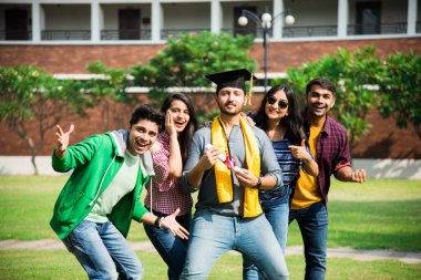 Arkadaşları dışarıda üniversite kampüsünde kutlama yaparken, Asyalı Hintli üniversite öğrencileri diploma alıyorlar.