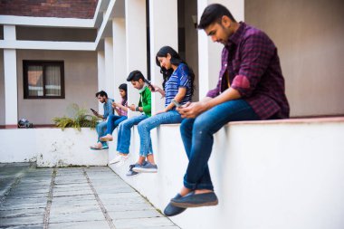 Üniversite kampüsünde otururken akıllı telefon kullanan Asyalı Hintli üniversite öğrencileri telefon bağımlılığını ortadan kaldırıyor.