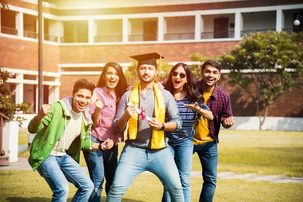 Asian Indian college students receives degree certificate while friends celebrates in college campus outdoors