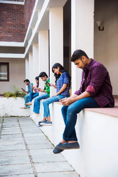 Asian Indian college students using smartphone while sitting in college campus, cel phone addiction