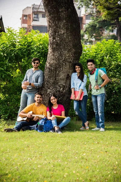 Asian Indian college students playing music with guitar while sitting in campus on stairs or over lawn