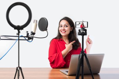 Pretty Indian woman speaks in front of microphone while recording a video blog for his subscribers, looking at camera clipart