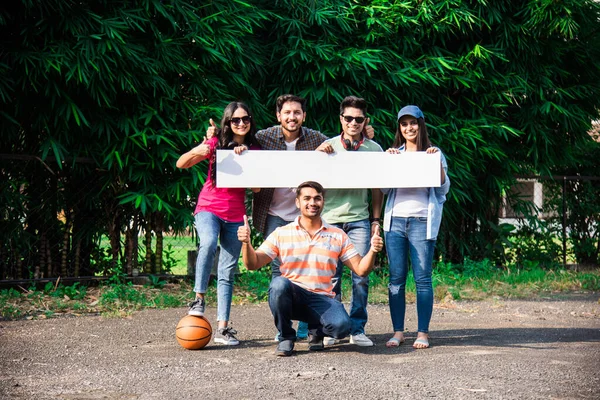 Asian Indian college students Holding or showing empty white board or placard in university campus, outdoor shot