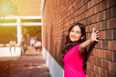 Asyalı Hintli üniversite öğrencisi dizüstü bilgisayar ya da kitap üzerinde çalışırken diğer sınıf arkadaşları arka planda üniversite kampüsünde açık havada resim çekiyor.
