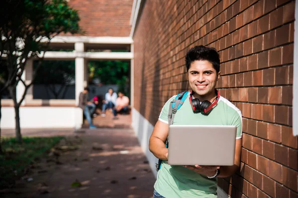 Asian Indian college student in focus working on laptop or reading book while other classmates in the background, outdoor picture in university campus