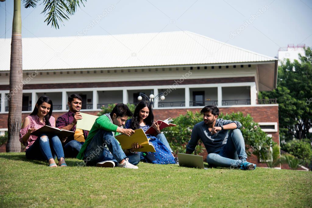 Young Asian Indian college students reading books, studying on laptop, preparing for exam or working on group project while sitting on grass, staircase or steps of college campus