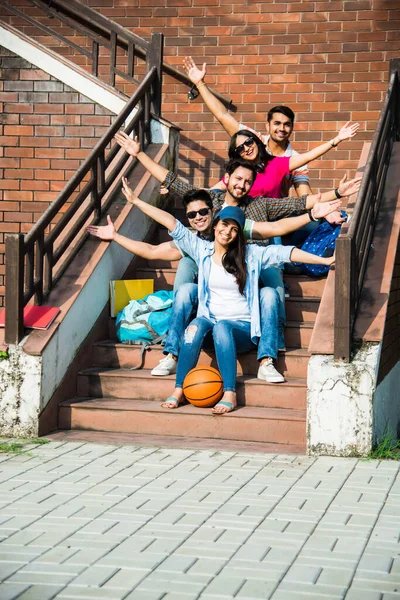 Cheerful Indian asian young group of college students or friends laughing together while sitting, standing or walking in campus
