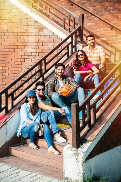 Cheerful Indian asian young group of college students or friends laughing together while sitting, standing or walking in campus