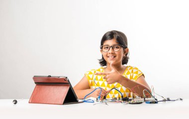 Elektronik deney - Asyalı Hintli küçük kız öğrenci kablolarla, bağlantılarla, dizüstü bilgisayarla veya tablet bilgisayarla bilim yapıyor veya okuyor