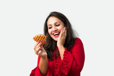 Genç Asyalı Hintli kadın beyaz arka planda dururken tatlı ve lezzetli Belçika waffle 'ı yiyor veya tutuyor.
