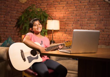 Asyalı Hintli çocuk evde bilgisayar ya da tablet kullanarak müzik ya da müzik aleti öğreniyor, hobiyi ikna ediyor