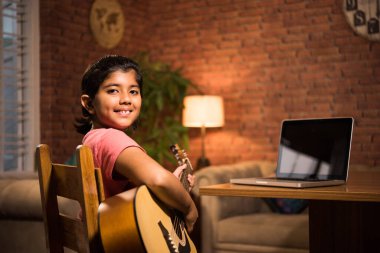 Asyalı Hintli çocuk evde bilgisayar ya da tablet kullanarak müzik ya da müzik aleti öğreniyor, hobiyi ikna ediyor