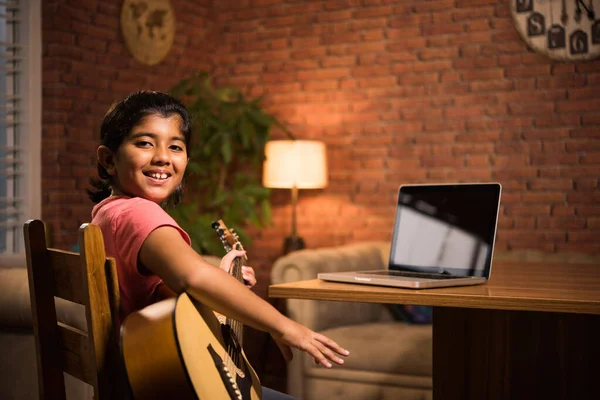 Asian Indian child learning music or musical instrument online using laptop computer or tablet at home, persuing hobby