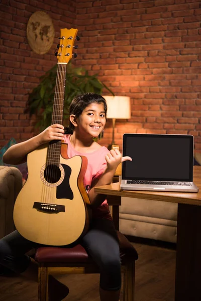 Asian Indian child learning music or musical instrument online using laptop computer or tablet at home, persuing hobby