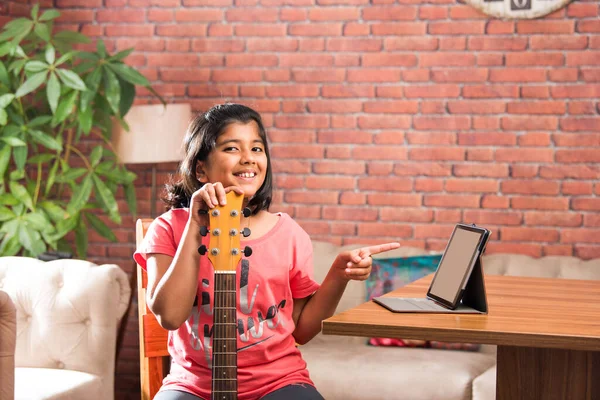 Asian Indian child learning music or musical instrument online using laptop computer or tablet at home, persuing hobby